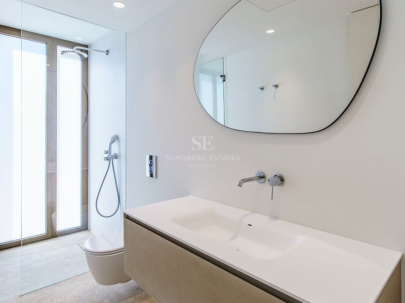 Salle de bain moderne dotée d'un miroir de forme organique, d'un meuble vasque blanc et de robinets chromés encastrés.