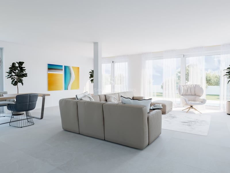 Salon minimaliste lumineux avec canapé beige, chaises de salle à manger bleues et grandes fenêtres sur le jardin.