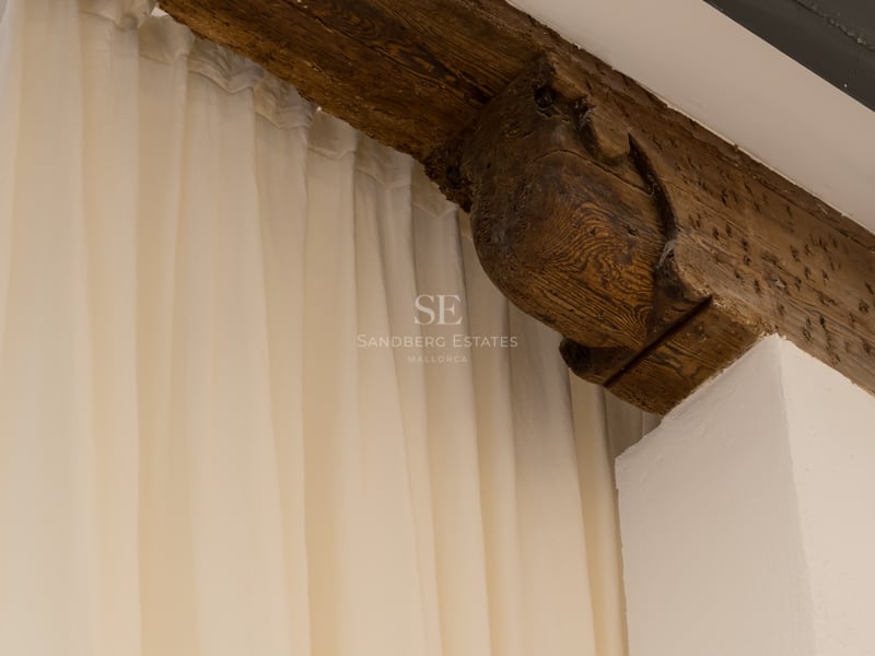 Poutre en bois sombre sculptée à la main à côté de rideaux crème et mur blanc.