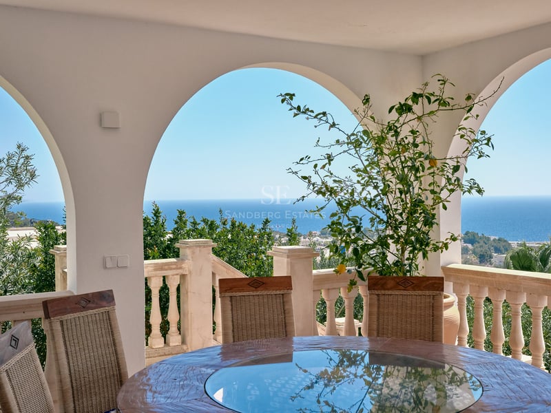 Terrasse couverte avec arches blanches, table ronde et balustrade en pierre surplombant la mer Méditerranée.