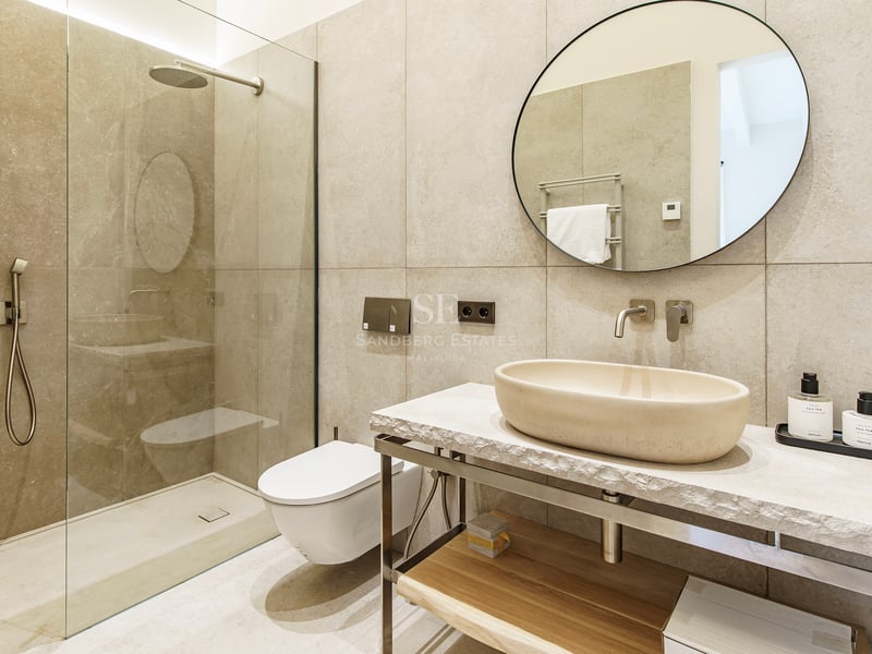 Baño contemporáneo con lavabo de piedra sobre encimera, espejo redondo y ducha de obra con mampara de cristal.