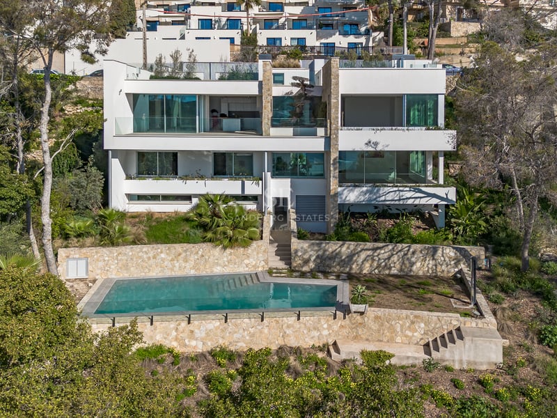 Vue extérieure d'une villa blanche à trois niveaux avec baies vitrées et piscine encadrée de murs en pierre.