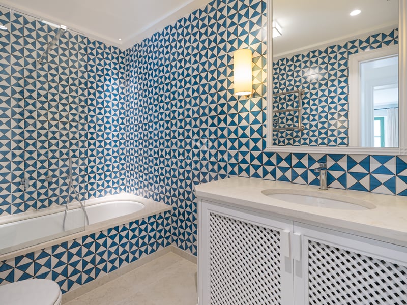 Salle de bain avec carrelage géométrique bleu et blanc, meuble vasque à claire-voie et baignoire intégrée.