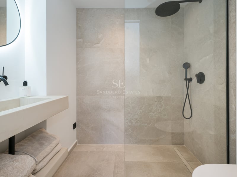 Salle de bain contemporaine avec douche vitrée, carrelage effet pierre et robinetterie noire mate.