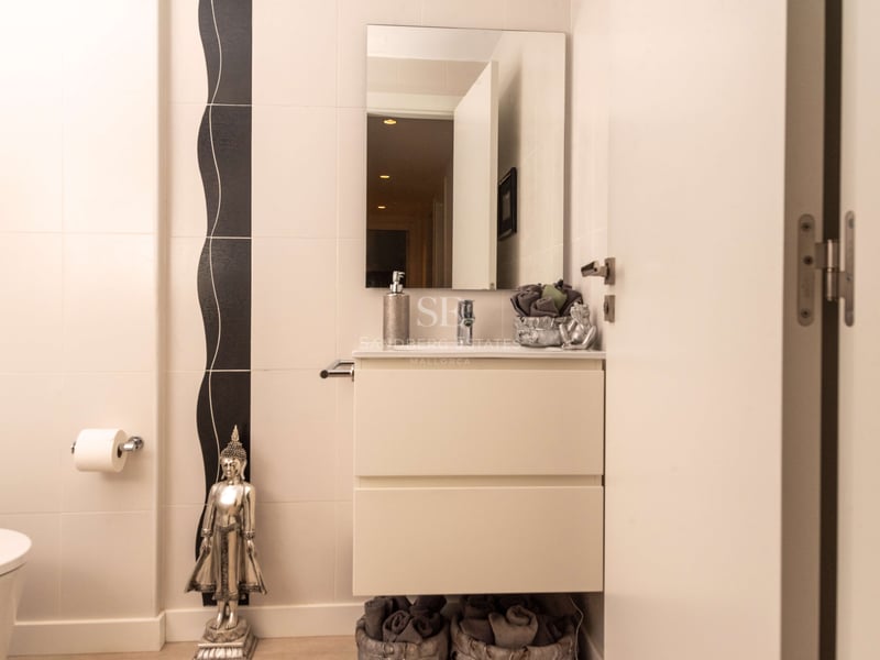 Salle de bains crème avec vanité suspendue blanche, miroir rectangulaire et statue de Bouddha argentée.