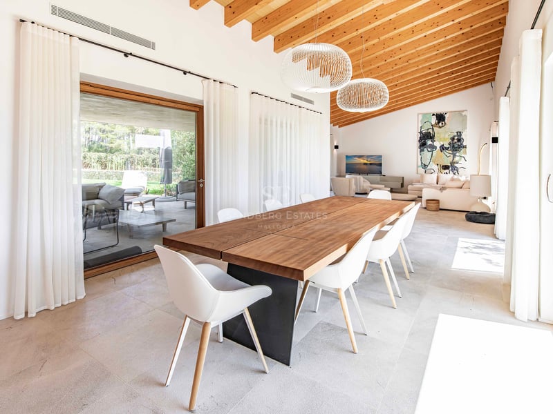 Salle à manger moderne avec table en bois, plafond voûté en bois et baies vitrées donnant sur la terrasse.