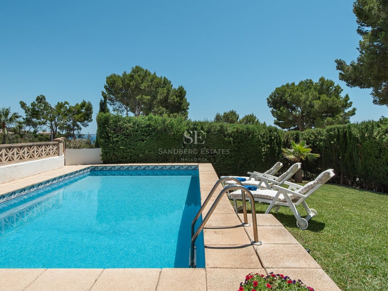 Une piscine rectangulaire aux eaux cristallines entourée d'une pelouse verte, de chaises longues et de hautes haies.
