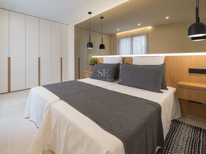 Chambre moderne avec placards blancs intégrés, tête de lit en bois avec éclairage et lits jumeaux.
