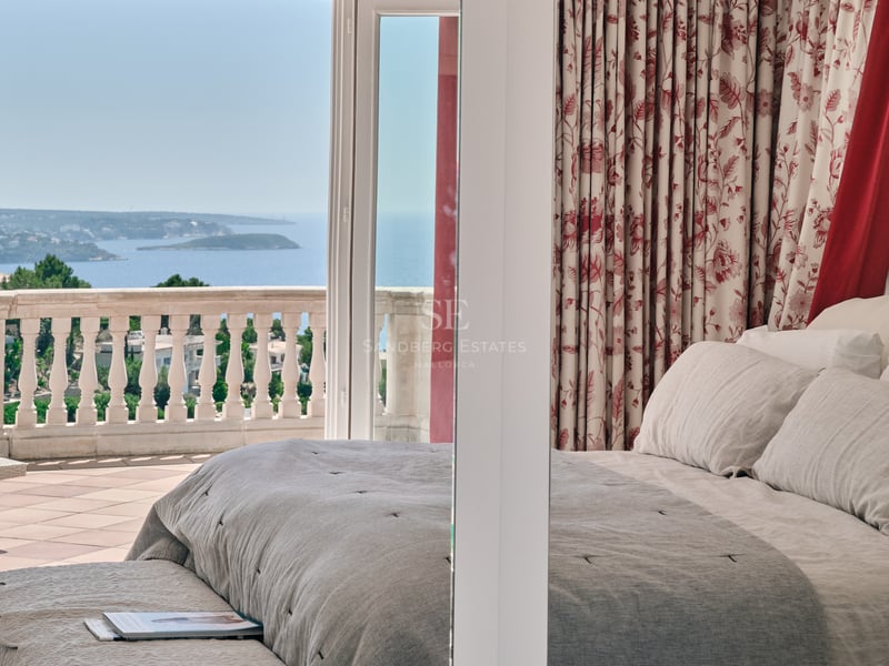 Chambre principale avec linge de lit neutre et terrasse en pierre offrant une vue panoramique sur la mer.