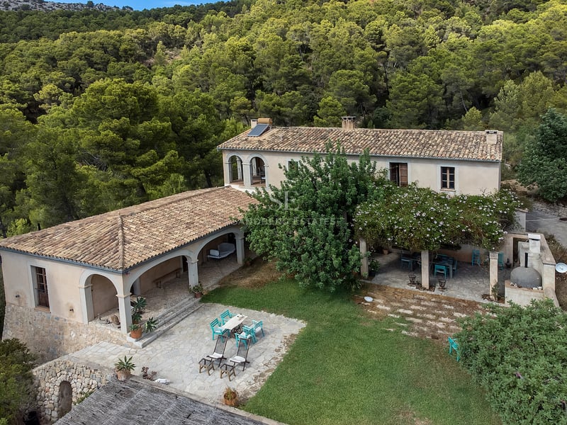 Vue aérienne d'une bastide traditionnelle en pierre avec toits en terre cuite au cœur d'une forêt de pins.