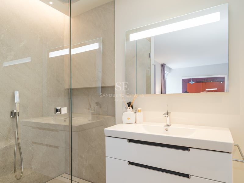 Salle de bain moderne avec meuble vasque blanc, grand miroir éclairé par LED et paroi de douche en verre.