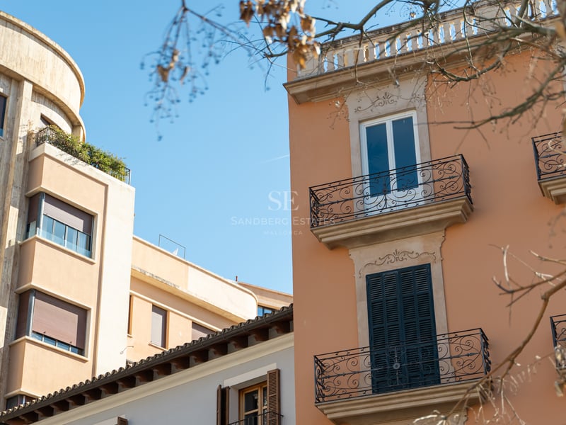 View of historic terracotta and stone building facades with wrought iron balconies against a clear blue sky.