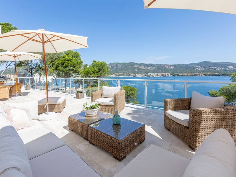 Terrasse ensoleillée avec mobilier en osier, parasols blancs et balustrade en verre surplombant la mer.
