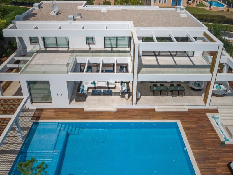 Vue aérienne d'une villa blanche contemporaine avec une grande piscine bleue, terrasse en bois et mobilier d'extérieur.