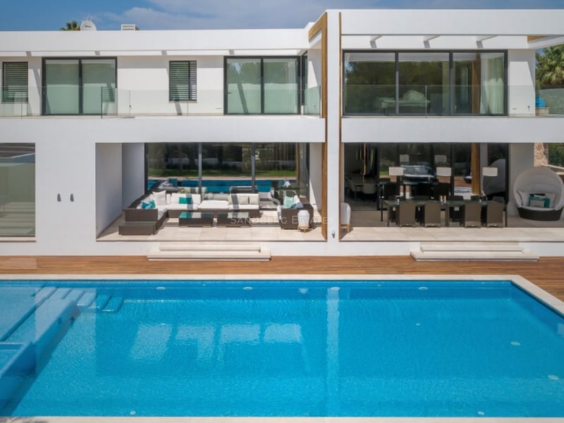 Vue arrière d'une villa contemporaine blanche sur deux niveaux avec piscine turquoise et salon d'été.