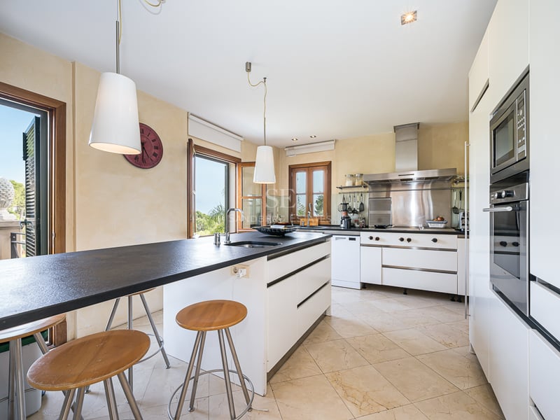 Cuisine moderne avec îlot central noir, tabourets en bois, plan de travail sombre et appareils en acier inoxydable.