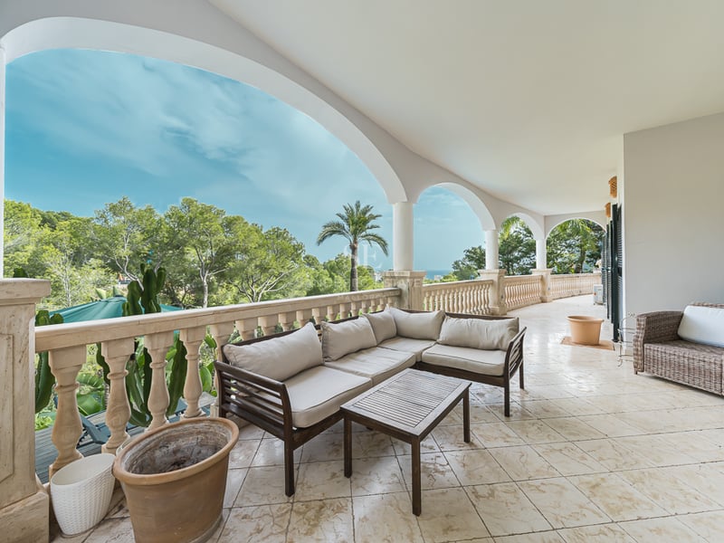 Vaste terrasse voûtée avec salon de jardin, balustrades en pierre et vue sur la végétation luxuriante et la mer.