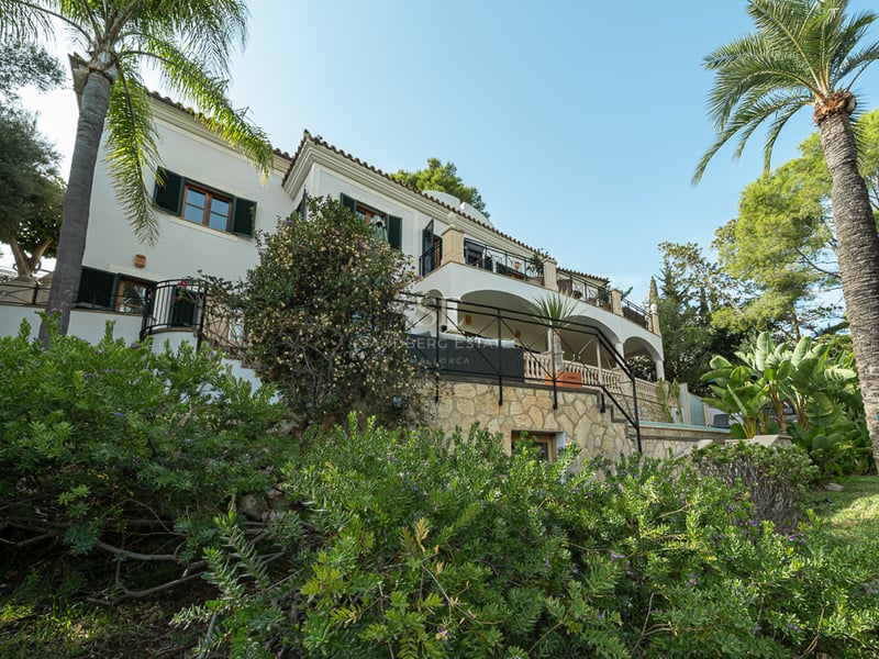 Villa blanche de trois étages avec terrasses voûtées, murs en pierre et palmiers sous un ciel bleu.