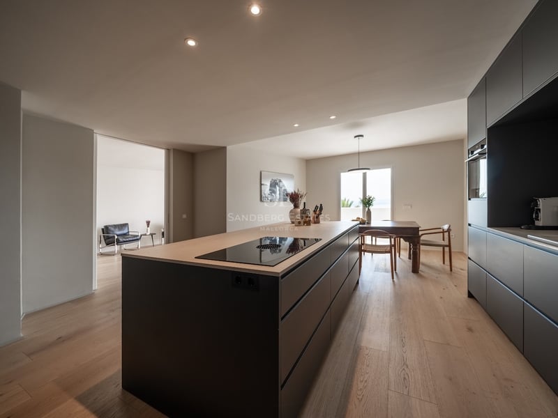 Cuisine moderne avec îlot anthracite, plan de travail en chêne, parquet et coin repas en arrière-plan.