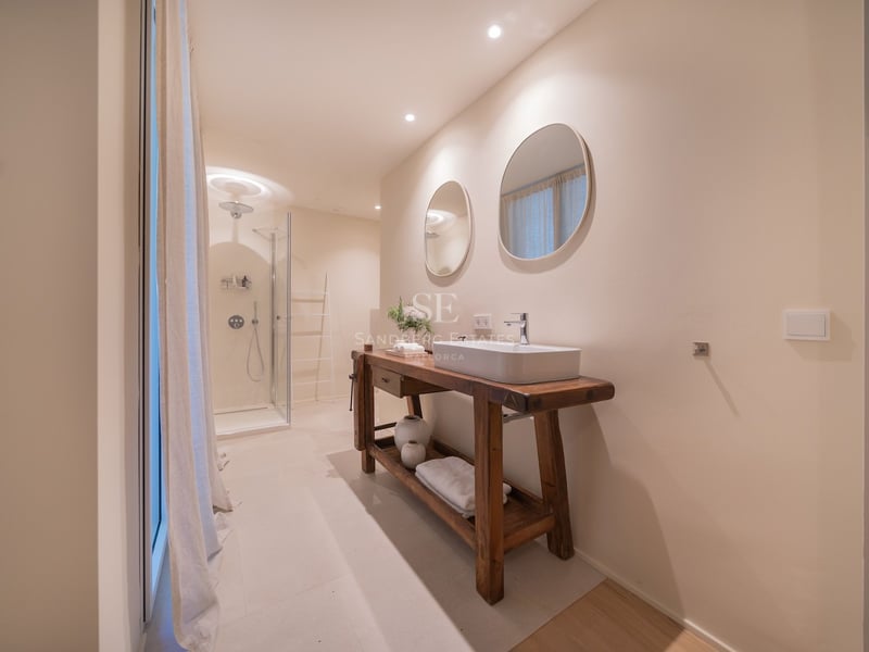 Salle de bains moderne avec meuble en bois massif, vasque à poser, miroirs ronds et douche vitrée.