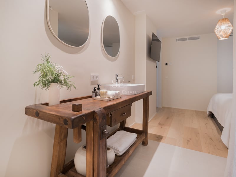 Salle de bain avec meuble en bois massif, vasque blanche et deux miroirs ovales sur mur blanc cassé.