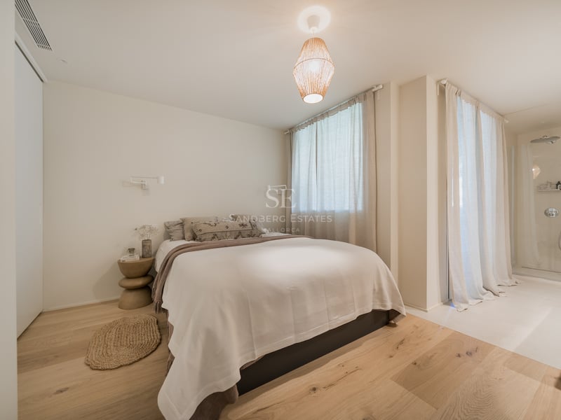 Chambre lumineuse avec parquet en chêne clair, literie crème et une suspension design en papier.