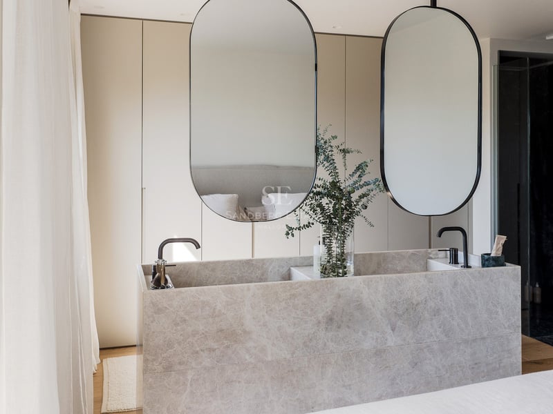 Double vasque moderne en pierre marbrée, deux miroirs ovales et robinetterie noire dans une salle de bain minimaliste.