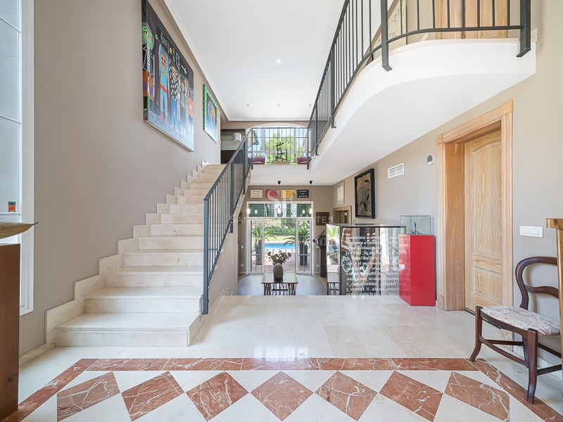Entrée de villa de luxe avec sol en marbre crème, incrustations en terre cuite et escalier élégant sous plafond haut.