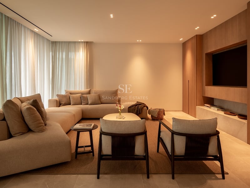 Salon élégant avec canapé modulaire beige, boiseries avec TV intégrée et éclairage chaleureux.
