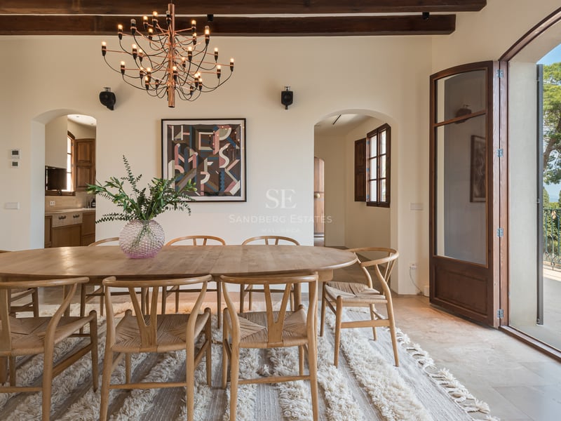 Table à manger ovale en chêne, chaises wishbone et poutres apparentes dans une luxueuse résidence méditerranéenne.
