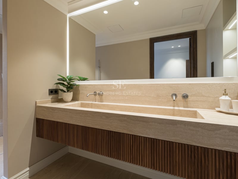 Luxury bathroom featuring a custom travertine integrated sink, fluted wood cabinetry, and a large backlit mirror.