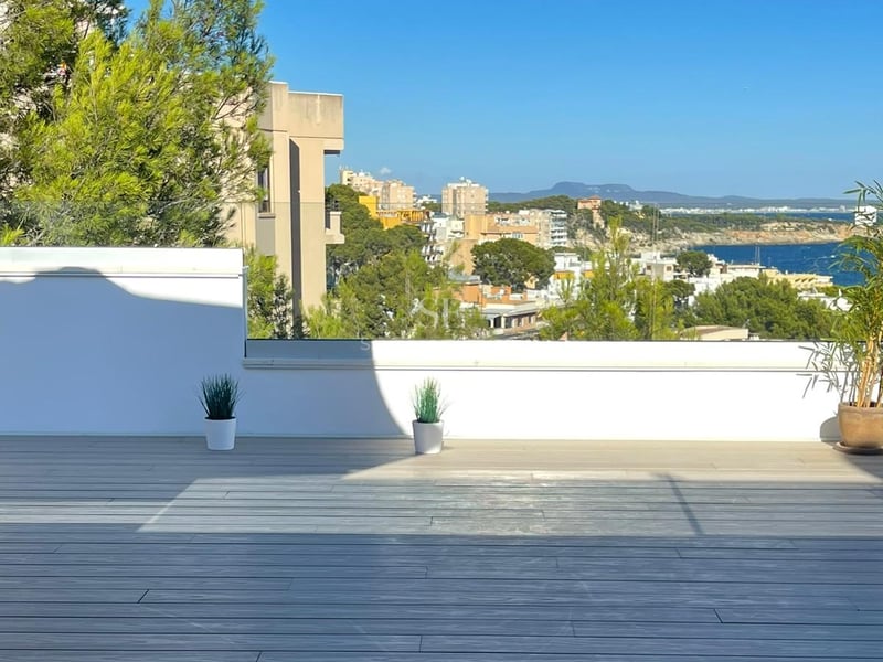 Terrasse en bois gris avec garde-corps en verre transparent surplombant une ville côtière et la mer Méditerranée.