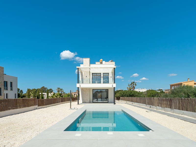 Piscine rectangulaire bleue menant à une villa moderne blanche de deux étages sous un ciel bleu pur.