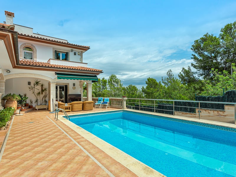 Grande piscine rectangulaire avec mosaïque bleue à côté d'une terrasse en terre cuite et d'une villa classique.