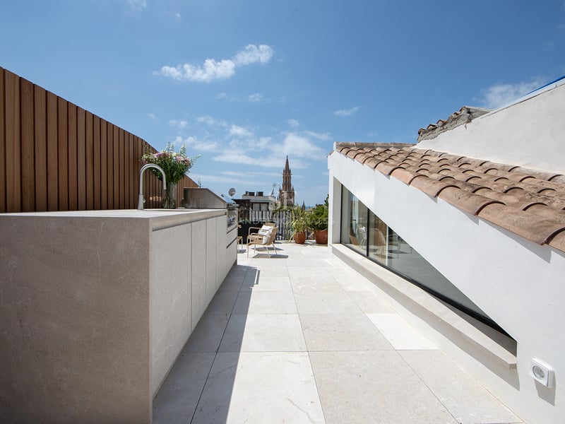 Terraza moderna en la azotea con cocina exterior, suelo de piedra y vistas a una catedral bajo un cielo azul.