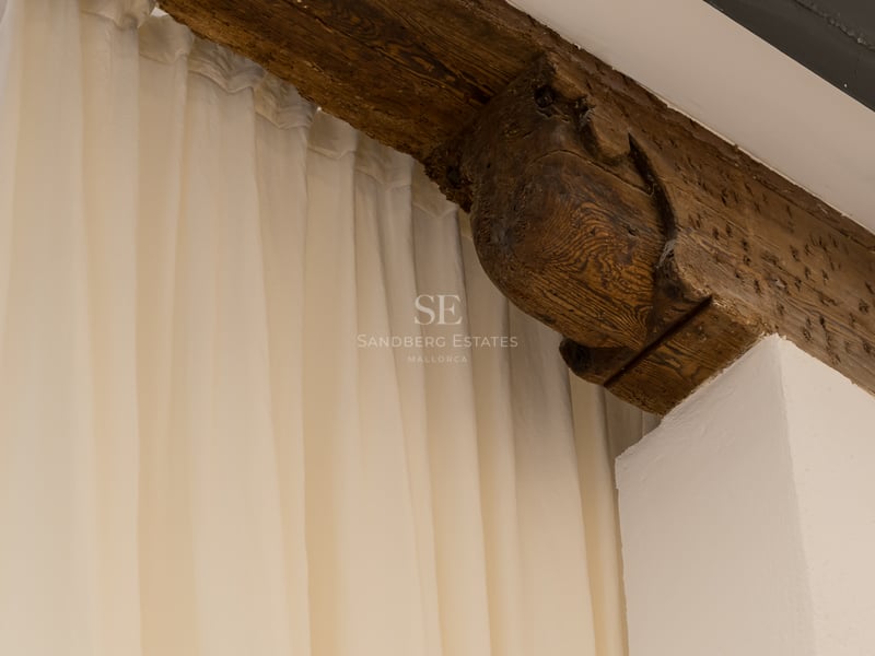 Gros plan d'un corbeau en bois sculpté à la main et d'une poutre sombre à côté de rideaux blancs fluides.
