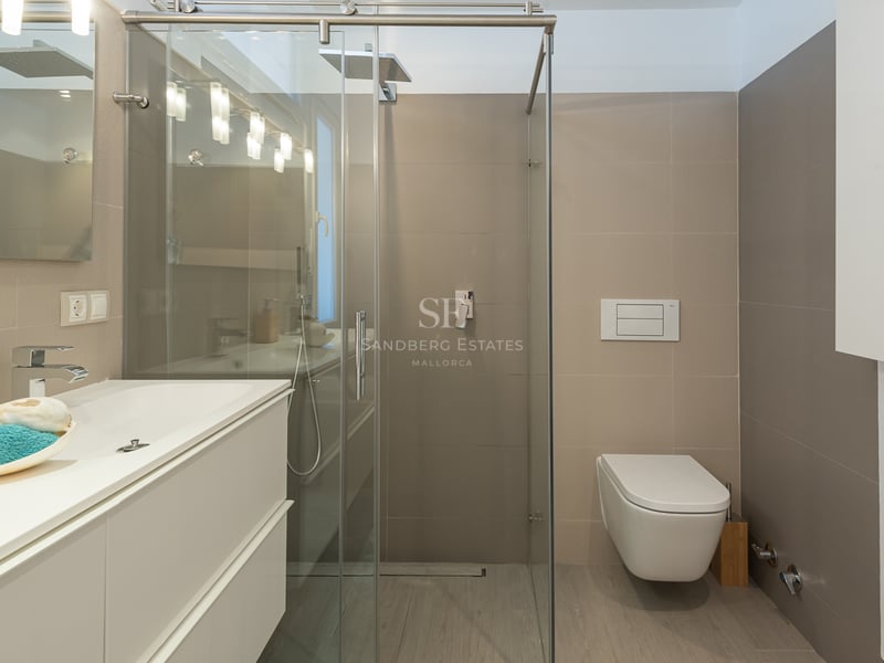 Salle de bain moderne avec meuble blanc, paroi de douche en verre et toilettes suspendues avec carrelage neutre.