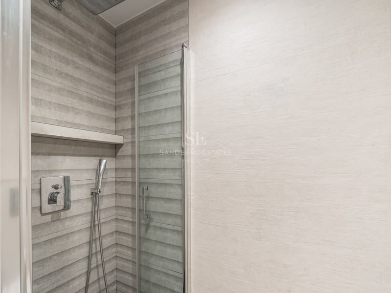 Douche moderne avec carrelage gris texturé, paroi en verre et robinetterie en chrome.
