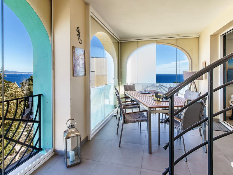Terrasse de salle à manger avec table en bois, rideaux de verre et vue sur la mer Méditerranée.