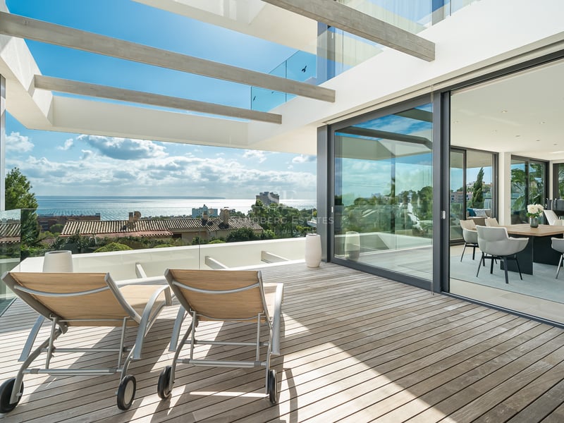 Chaises longues sur une terrasse en bois avec garde-corps en verre surplombant la mer, à côté d'une salle à manger ouverte.