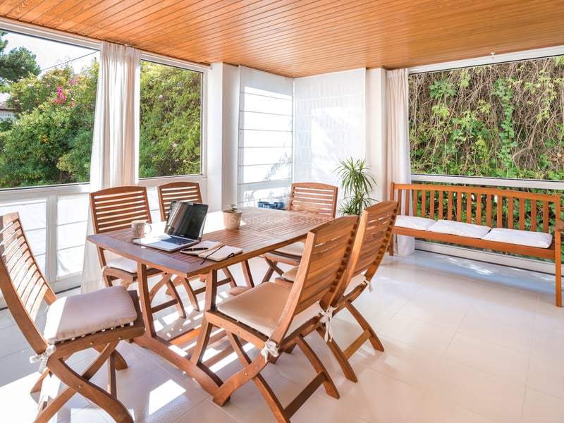 Une terrasse ensoleillée avec table à manger en bois, chaises et banc, donnant sur la verdure du jardin.