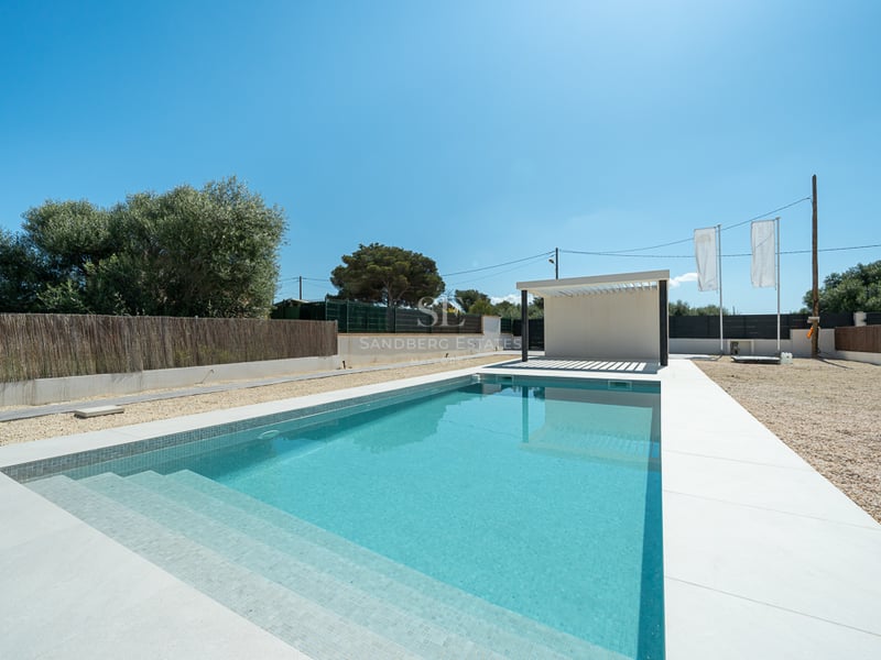 Piscine rectangulaire turquoise avec bordure blanche et pergola moderne sous un ciel bleu pur.