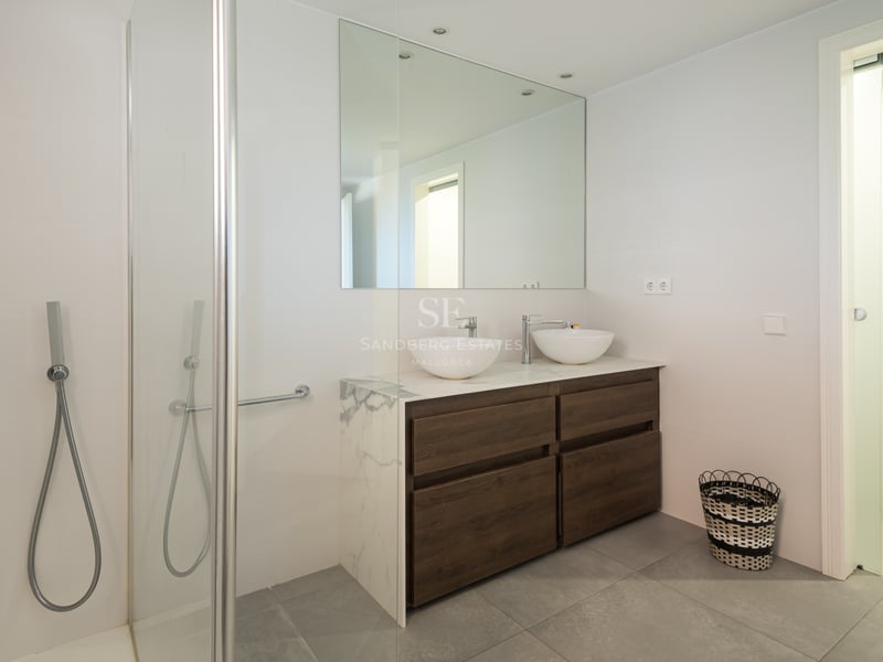 Salle de bain moderne et lumineuse avec meuble double en bois, plan en marbre, deux vasques et douche en verre.