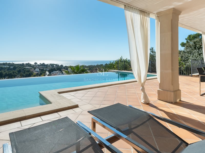 Piscine à débordement sur terrasse en terre cuite avec vue sur la Méditerranée et coin repas ombragé.