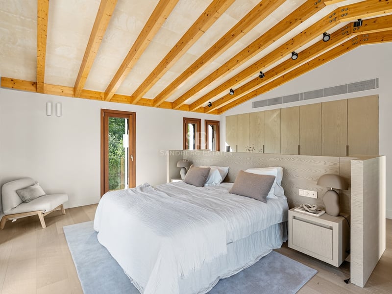 Modernt master bedroom med snedtak, träbalkar, stor säng och inbyggda garderober.