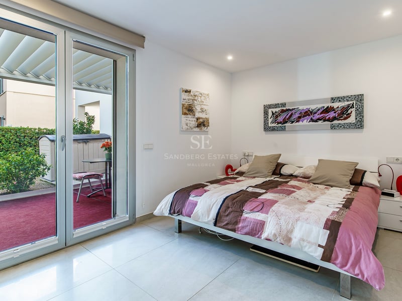 Chambre lumineuse avec un lit double, de l'art moderne et une grande porte vitrée coulissante ouvrant sur une terrasse.