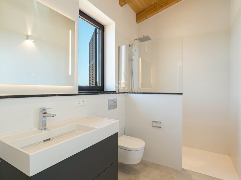 Baño blanco moderno con ducha a ras de suelo, mueble suspendido, espejo LED y vigas de madera natural.