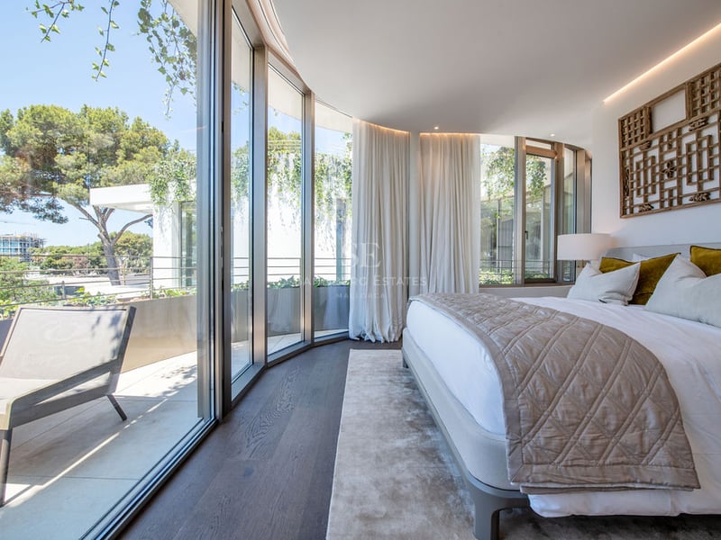 Chambre de maître contemporaine avec murs en verre incurvés, parquet en bois foncé et accès à une terrasse privée.
