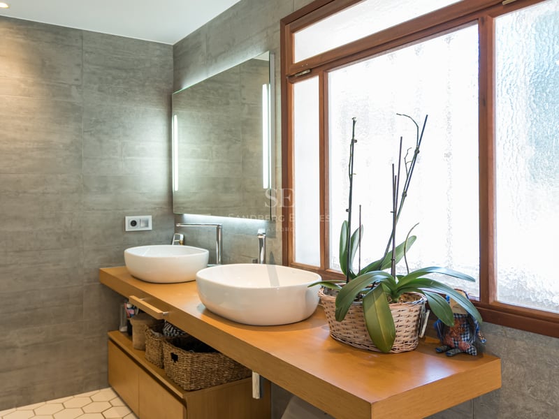 Salle de bain moderne avec deux vasques blanches sur meuble en bois, murs gris et miroir rétroéclairé.