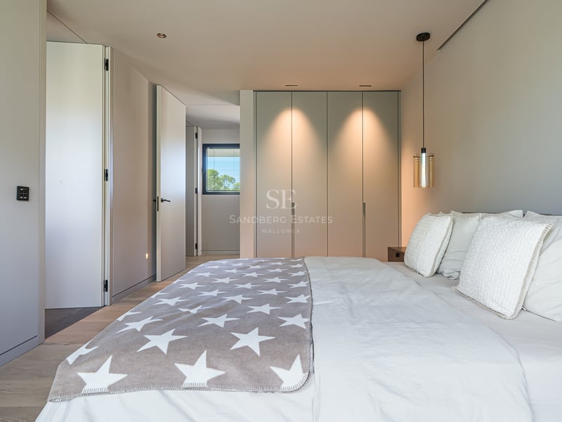 Chambre moderne et lumineuse avec un grand lit, un jeté de lit gris à étoiles et des placards intégrés avec éclairage chaud.